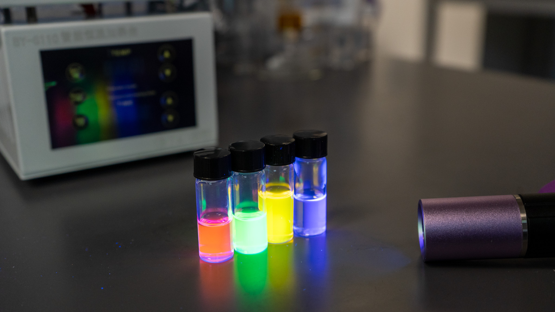 Full-colour CPL achieved in solution: red, green, yellow, and blue dye samples fluoresce under UV, illustrating the platform’s broad visible spectrum capability.