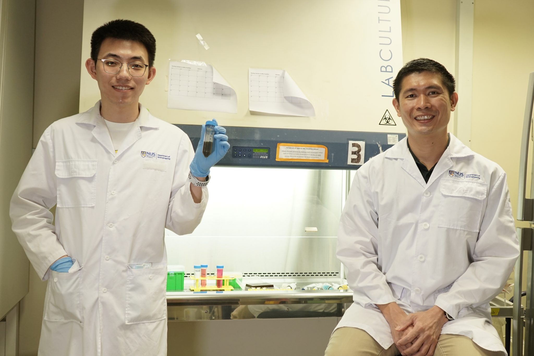 Dr James Kah Chen Yong (right) and PhD student Lin Yuanzhe with a vial of nanoparticles coated in polydopamine (PDA) by Dr Kah’s method.