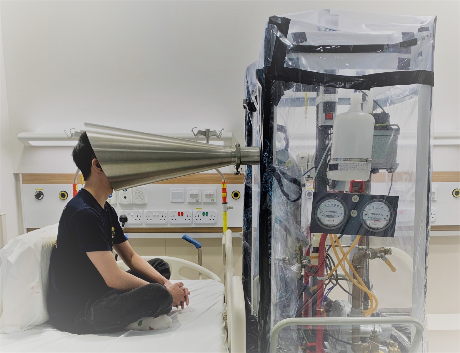 NUS researcher Mr Douglas Tay in a hospital room at the NCID demonstrating how the Gesundheit II exhalation collection equipment is used.